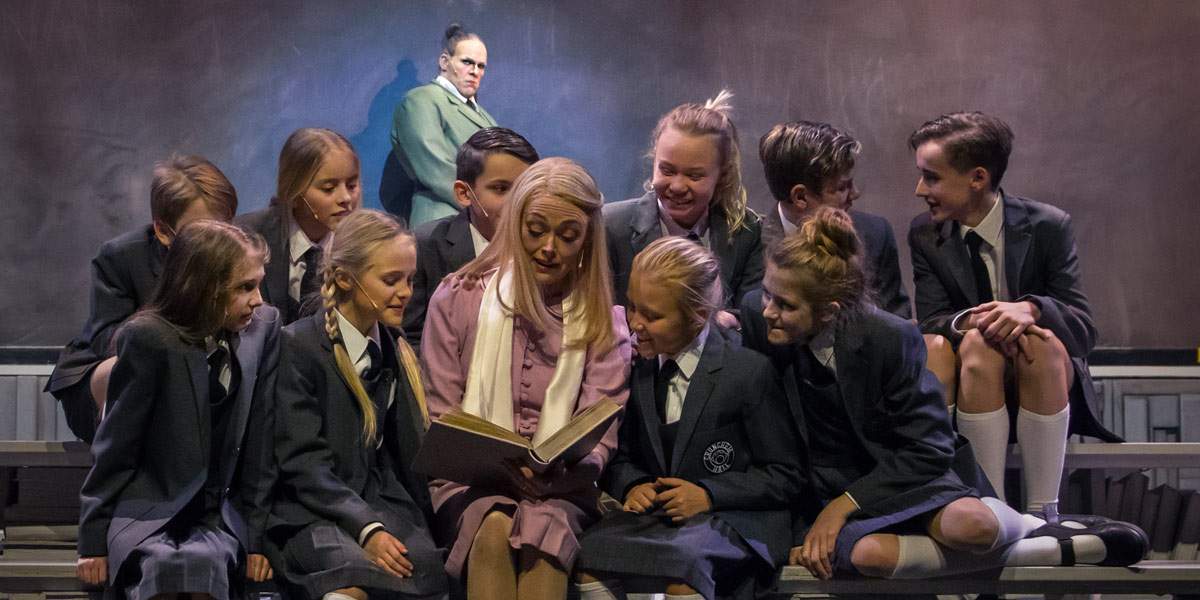Fröken Honey med sin klass och Rektor Trunchbull i bakgrunden.